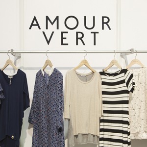 Amour Vert at Stitch showing a swath of clothing on hangers against a white backdrop.