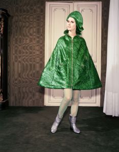 Grass-green rain cape, in embossed with relief print. Industrial, by Pierre Cardin, brass zipper, brass buttons on pockets, standing collat, matching beret (chasseur) on . Green nylon stockings, and short, silver-colored rubber boots1960's Fashion, France