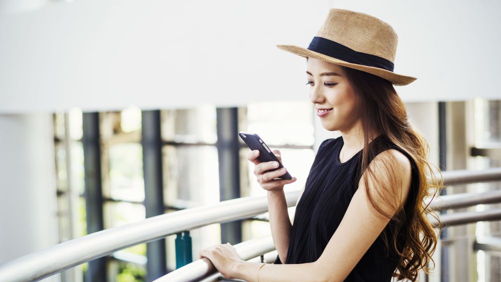 MODEL RELEASED Young woman with long brown hair, wearing a Panama hat, in a shopping centre, using a mobile phone.VARIOUS