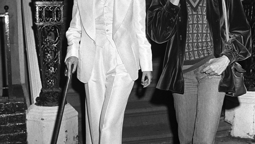 Bianca Jagger and Nathalie Delon attend a party thrown by Kenny Lane in a Murray Hill townhouse.  Jagger wears a white Halston suit and walks with a cane