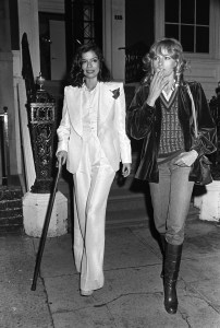 Bianca Jagger and Nathalie Delon attend a party thrown by Kenny Lane in a Murray Hill townhouse.  Jagger wears a white Halston suit and walks with a cane