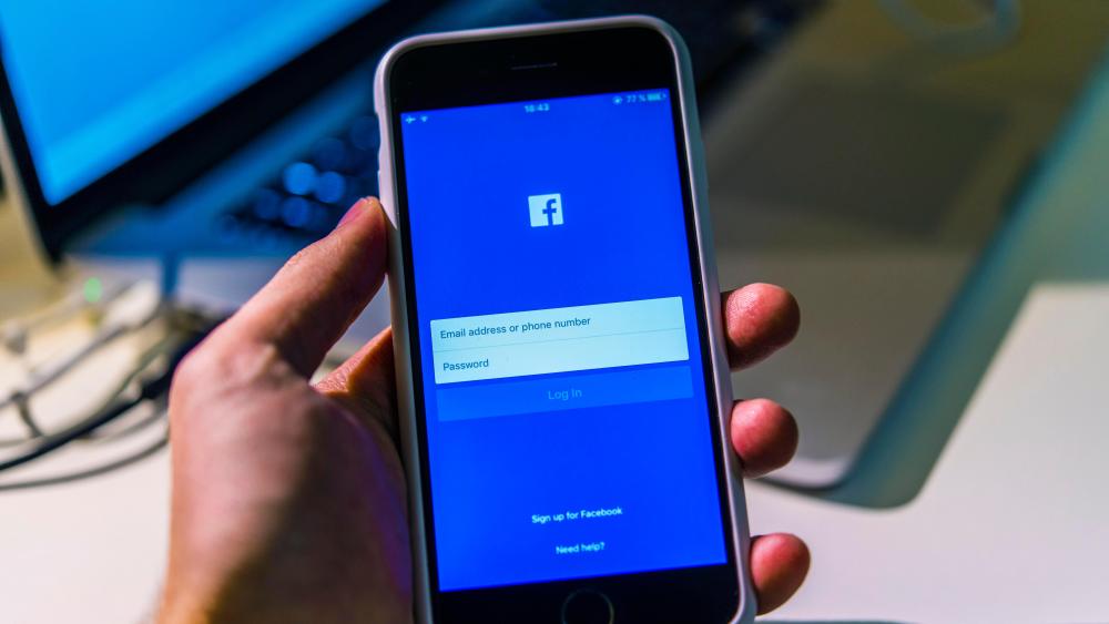 Hand holding iPhone 6S with open Facebook app on screenVARIOUS