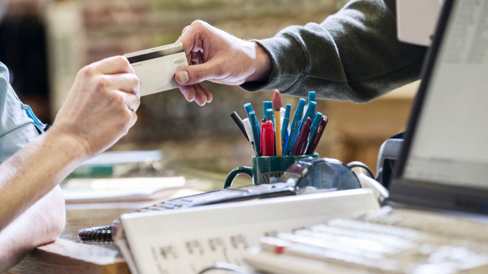 MODEL RELEASED Closeup of hands exchanging a credit card during a retail sale next to a computer at the front desk of a retail shop.VARIOUS