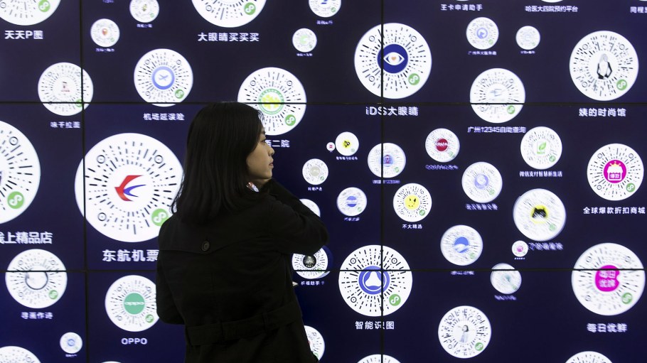 An attendee stands in front of a screen displaying QR codes for various programs and services at Tencent Holdings Ltd.'s WeChat Open Class Pro conference in Guangzhou, China, on Monday, Jan. 15, 2018.