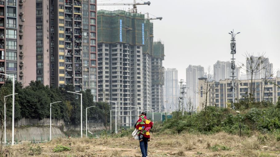 A man carrying a child on his back walks on a field near new housing developments on the outskirts of Chongqing, China,
