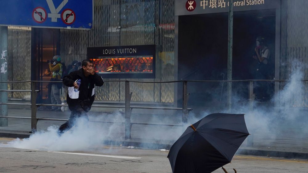 A man runs away from tear gas fired by riot police in Central in Hong Kong, in front of a Louis Vuitton store.