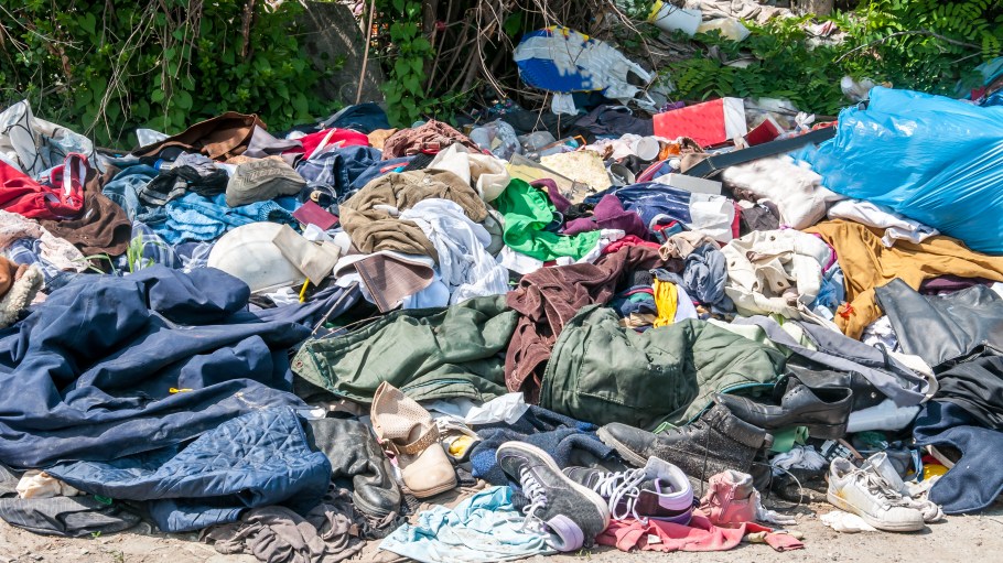 Pile of old clothes and shoes dumped on the grass as junk and garbage, littering and polluting the environment