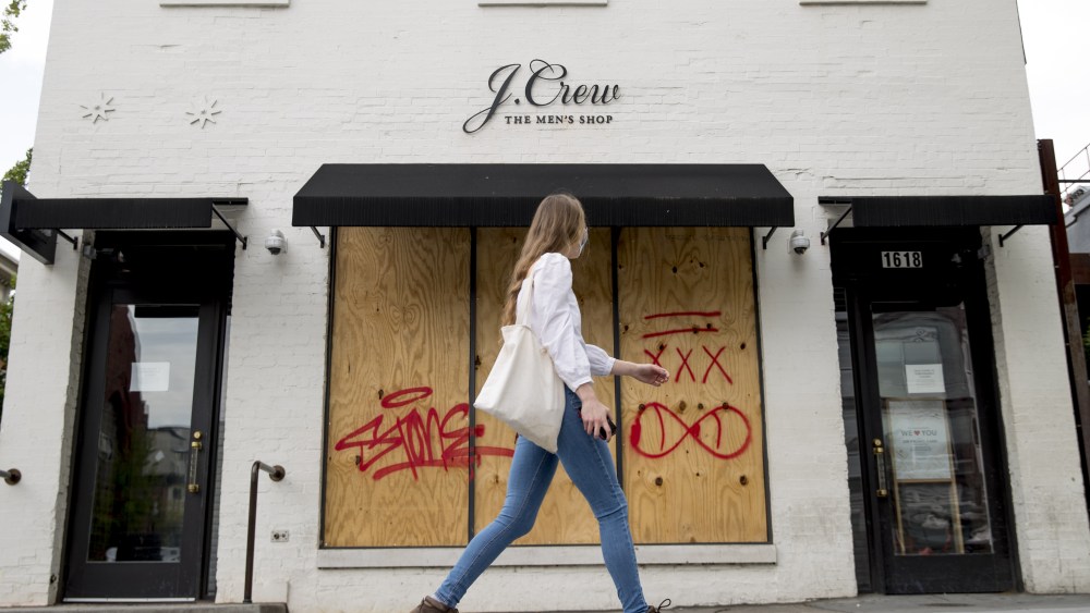 woman walks past a boarded up J. Crew