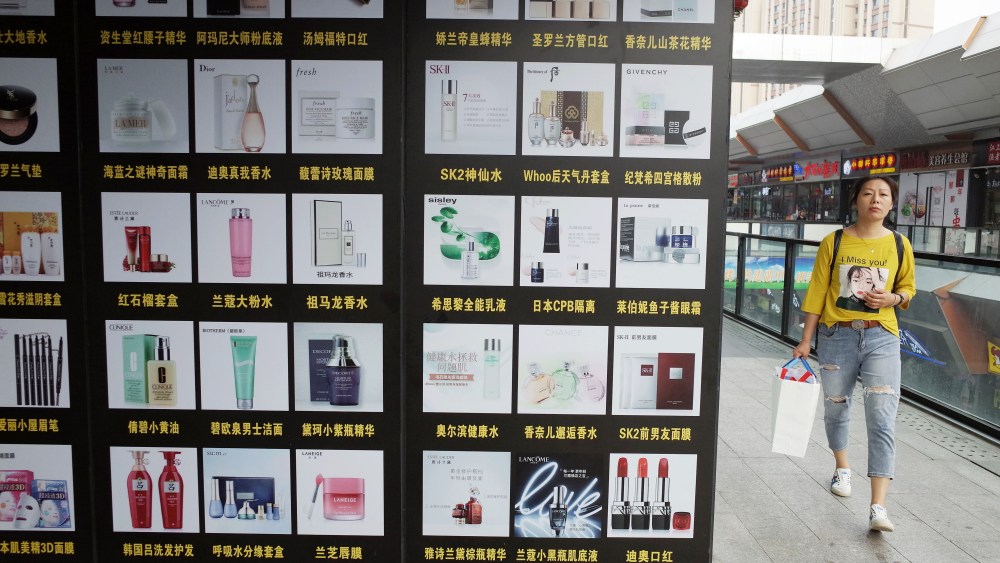 A woman walks past posters showing cosmetics outside a shopping mall in Beijing, China.