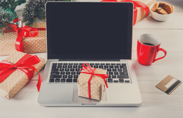 Christmas online shopping. Laptop with copy space on screen lay on white wood, present boxes and christmas tree on background. Internet commerce on winter holidays concept