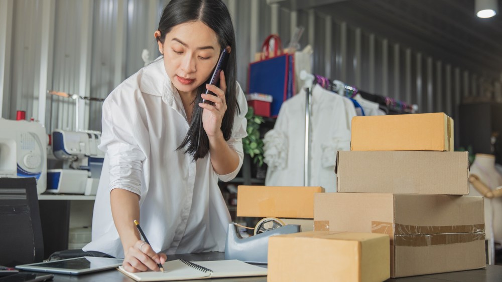 Young business woman working online e-commerce shopping at her shop. Young woman seller prepare parcel box of product for deliver to customer. Online selling, e-commerce.