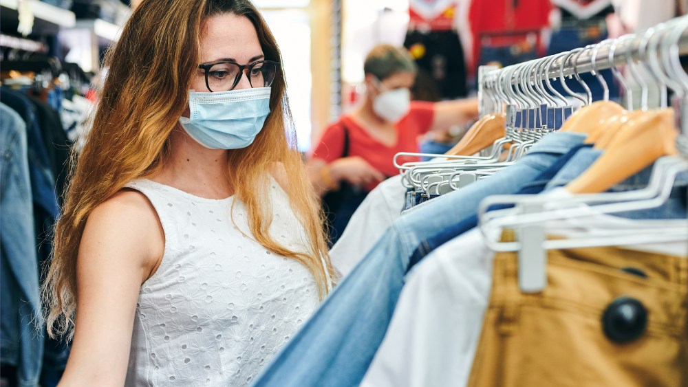 Woman in a safety mask looking at clothes in a shop. New post covid-19 normality