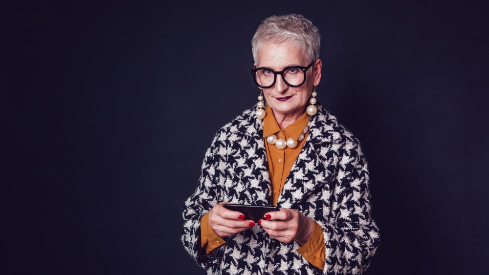 Stylish old woman in glasses using smartphone on a black background.