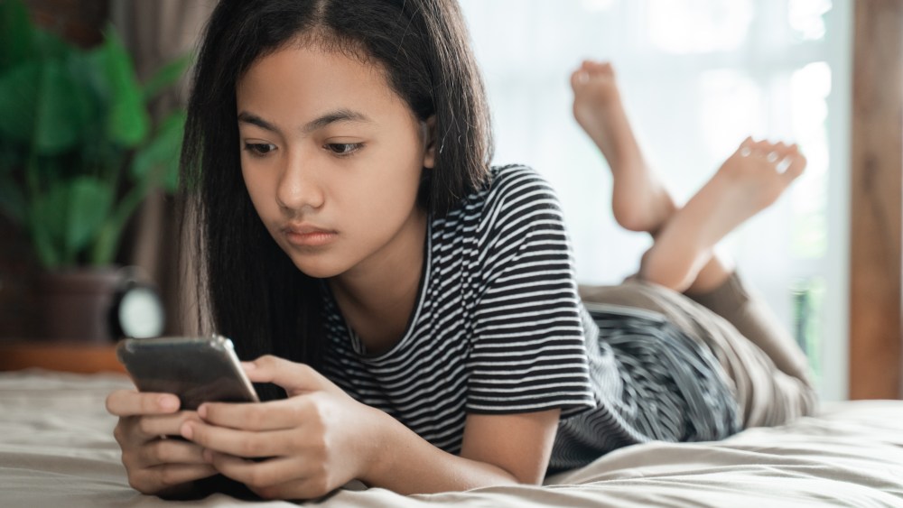 teenager using mobile smart phone at home while laying on the bed