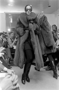 Model Pat Cleveland walks the runway in a fur coat and sunglasses from Halston's fall 1977 ready to wear collection.