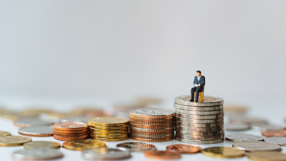 Miniature people, businessman sitting on stack coins using as business and financial concept
