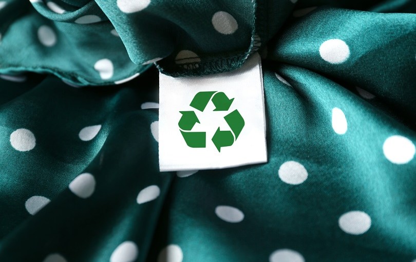 Clothing label with recycling symbol on green garment, closeup