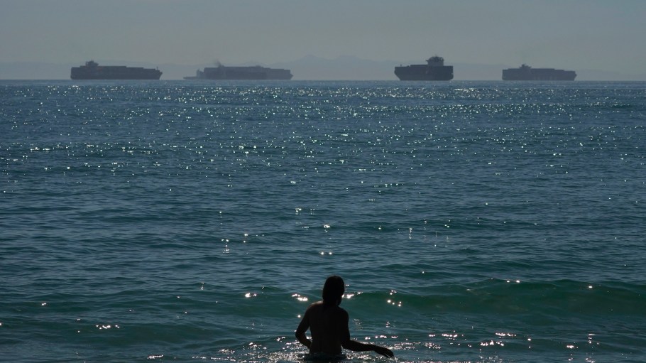 A man wades through the water at Seal Beach Calif., as container ships waiting to dock at the Ports of Los Angeles and Long Beach are seen in the distance.