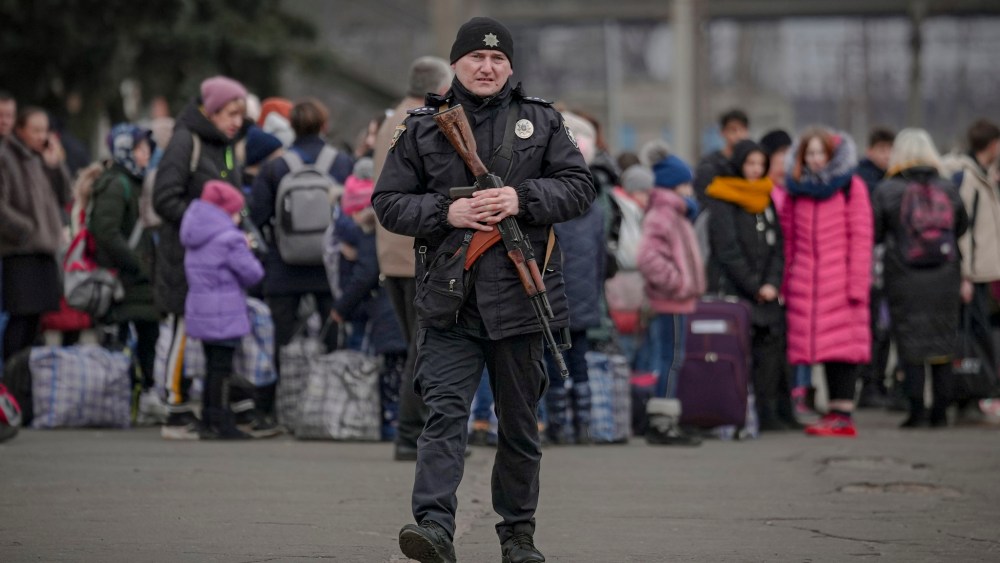 A Ukrainian police officer carrying an assault rifle walks on a platform backdropped by people waiting for a Kiev bound train in Kostiantynivka, Donetsk region, eastern Ukraine, Thursday, Feb. 24, 2022.
