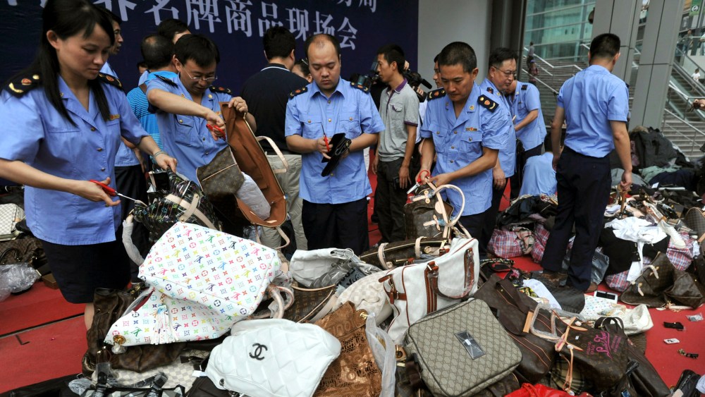 Chinese business administration officers cut fake Louis Vuitton handbags during a mass elimination of counterfeit Louis Vuitton products.