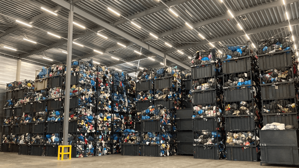 Stacked boxes and bins of clothing and textile waste fill a facility.