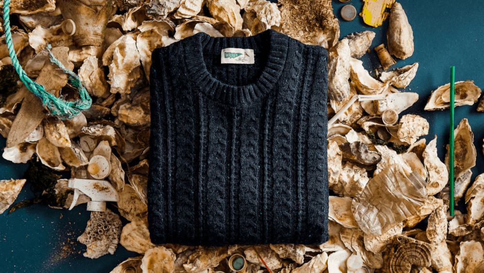 A navy blue Huckberry sweater made with SeaWool sits atop oyster shells.
