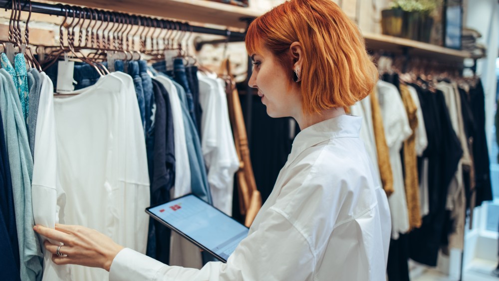 Woman taking inventory on digital tablet in clothing store. Woman manager in a fashion retail store using a tablet for working and checking the shop stock.