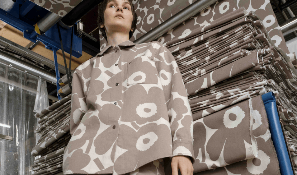 An androgynous model sports a neutral-toned poppy print Marimekko jacket and trouser against bolts of fabric.