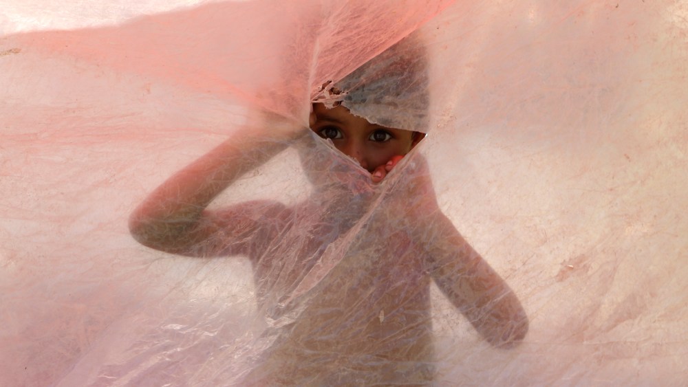 A displaced boy peeks through a hole in a plastic shelter after fleeing his flood-hit home on the outskirts of Peshawar, Pakistan, Sunday, Aug. 28, 2022. Officials in Pakistan say deaths from widespread flooding have topped 1,000 since mid-June and the country's climate minister called the deadly monsoon season "a serious climate catastrophe." Flash flooding from the heavy rains has washed away villages and crops as soldiers and rescue workers evacuated stranded residents to the safety of relief camps and provided food to thousands of displaced Pakistanis. (AP Photo/Mohammad Sajjad)