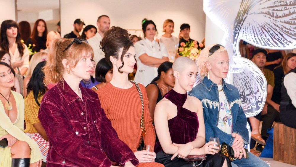 Guests, many with the Stella McCartney Falabella bag or Mylo derivative, are seen attentively listening during a panel conversation.