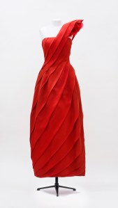 A red dress with one sharp shoulder drapes in a pattern of fluid lines from Valentino Haute Couture Spring-Summer 1981, mod 262.