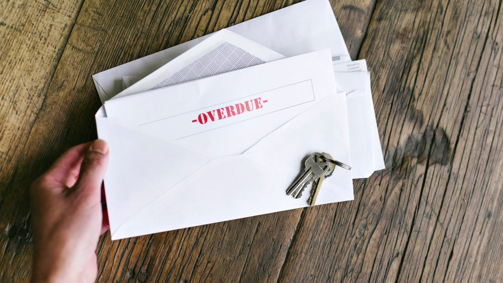Hands of a woman hold an letter with that reads Overdue in an envelope - Keys - Table - Late Payment