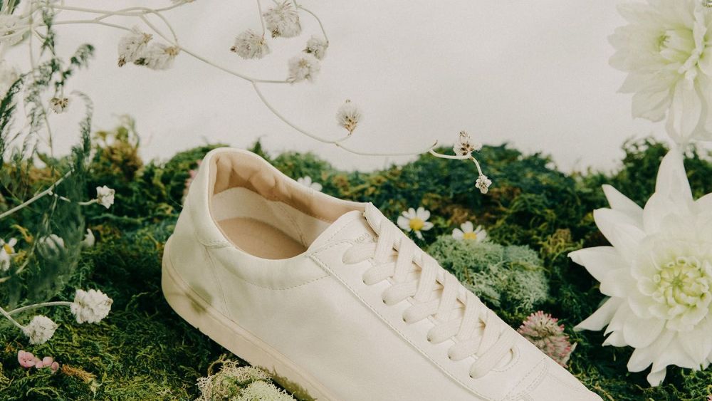 A Look at Koio’s Mello sneaker in white shot atop a mossy backdrop with white flowers.