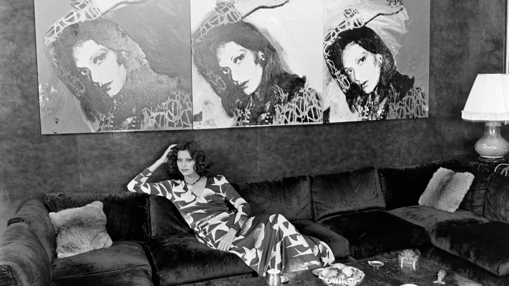 Model wears a Diane von Furstenberg seagull-printed wrap dress and poses in the designer's apartment. An Andy Warhol portrait of Diane von Furstenberg adorns the wall of her living room. (Photo by Pierre Schermann/WWD/Penske Media via Getty Images)
