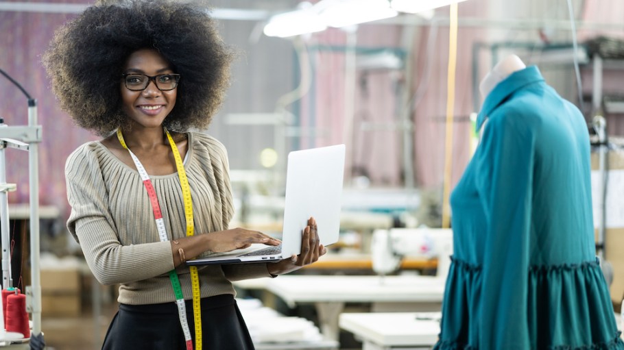Fashion designer creating new products in factory and using laptop.