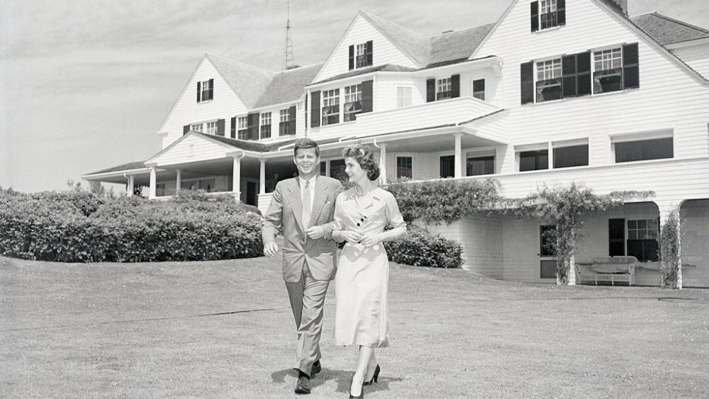 Senator John F. Kennedy and Jacqueline Bouvier stroll across the lawn of his family's home after announcing their engagement.