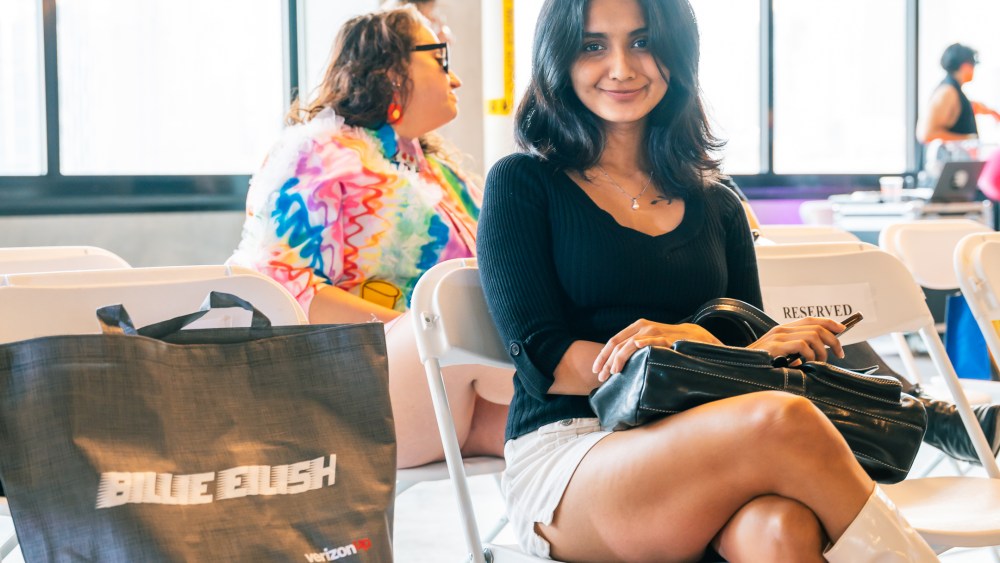 At Fashion Week Brooklyn, a show goer sits with a smile next to a tote bag that says "Billie Eilish."