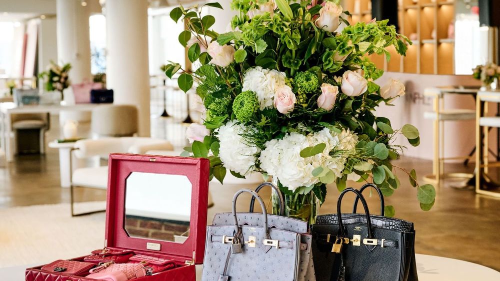 A lineup of Fashionphile bags in red, grey and black. In the back a view of roses and peonies.
