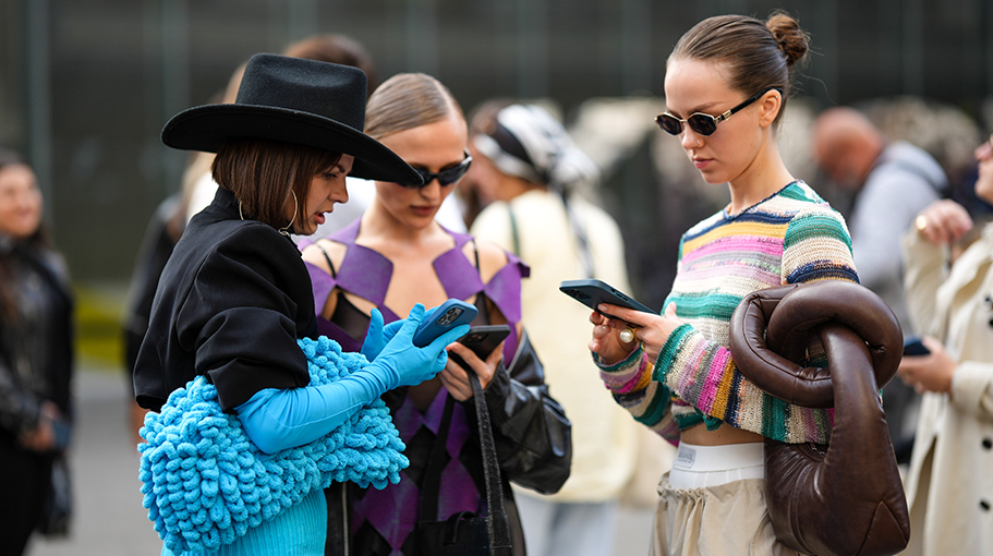 A guest (L) wears a black felt hat, a black top, silver oversized earrings, a black cropped blazer jacket, a blue flashy wool midi skirt, black pants, blue flashy wool gloves, a matching blue flashy fringed puffy handbag, a guest (R) black sunglasses, a pale multicolored striped print pattern wool knot pullover, dark brown shiny leather puffy knot large handbag, a white boxer, beige large wide legs pants, gold rings, outside Missoni, during the Milan Fashion Week - Womenswear Spring/Summer 2023 on September 23, 2022 in Milan, Italy.