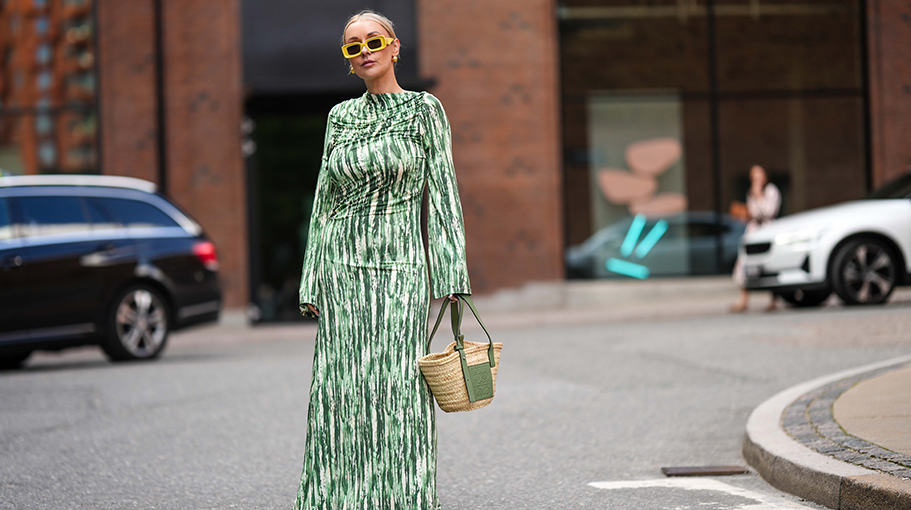 Justyna Czerniak wears yellow squared sunglasses from Loewe, gold earrings, a green and white latte marble print pattern high neck / long sleeves / long tube dress, a beige wicker and green khaki shiny leather basket handbag from Loewe, khaki dark shiny varnished plastic shoes, outside Lovechild 1979 , during the Copenhagen Fashion Week Spring/Summer 2024 on August 08, 2023 in Copenhagen, Denmark.