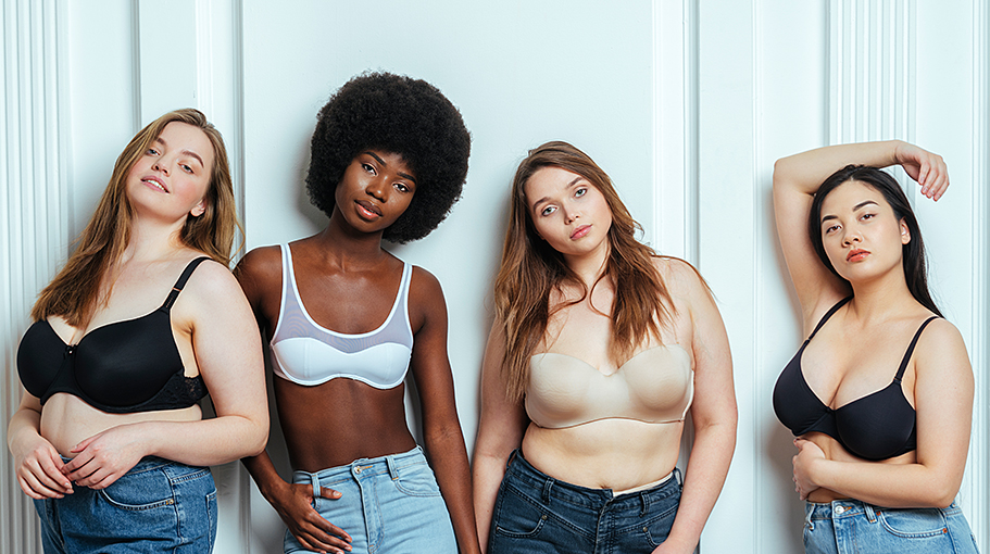 Multi-ethnic group of female models wearing bras and jeans posing against wall - stock photo
