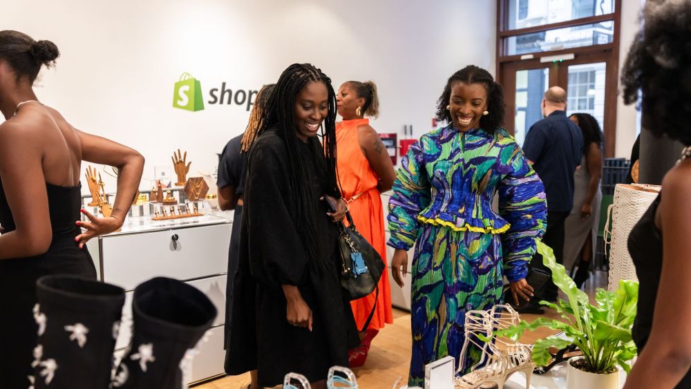 At the Shopify store, Amira Rasool in a pleated colorful dress engages with attendees at The Folklore Connect's NYFW showroom.