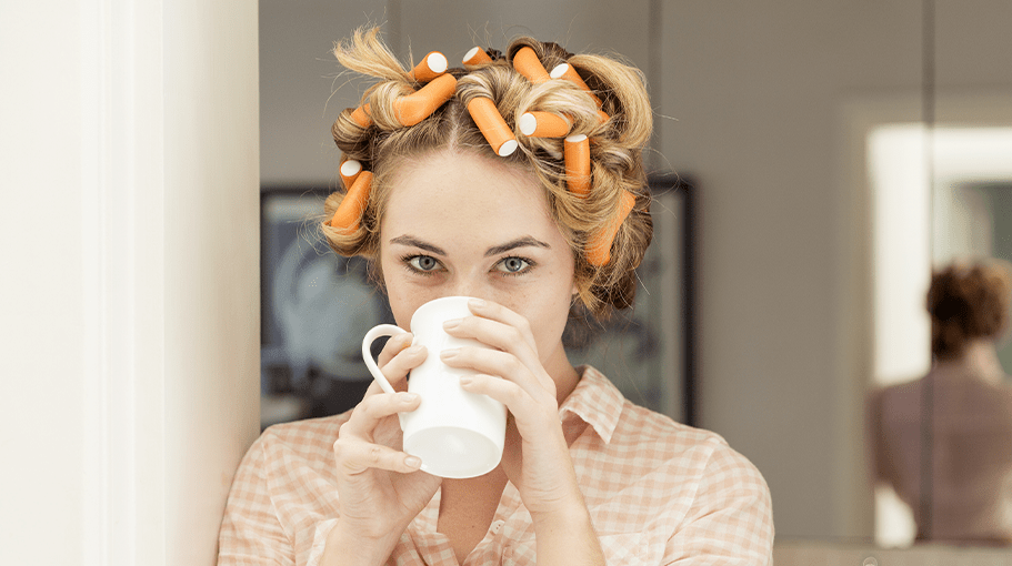 Portrait of young woman with curlers in hair drinking coffee - stock photo