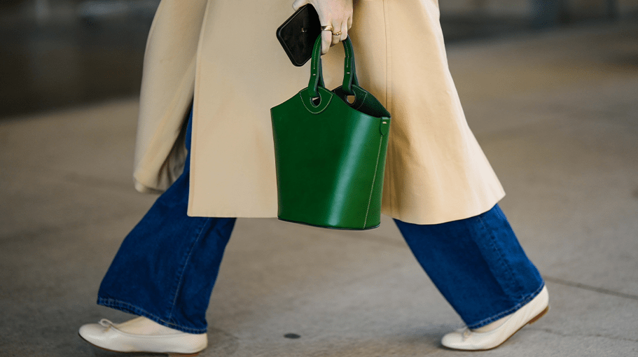 NEW YORK, NEW YORK - FEBRUARY 10: A guest wears a gold ring, a beige long coat, navy blue denim large pants, a green shiny leather handbag, beige shiny leather ballerinas , outside Kate Spade, during New York Fashion Week, on February 10, 2023 in New York City. (Photo by Edward Berthelot/Getty Images)