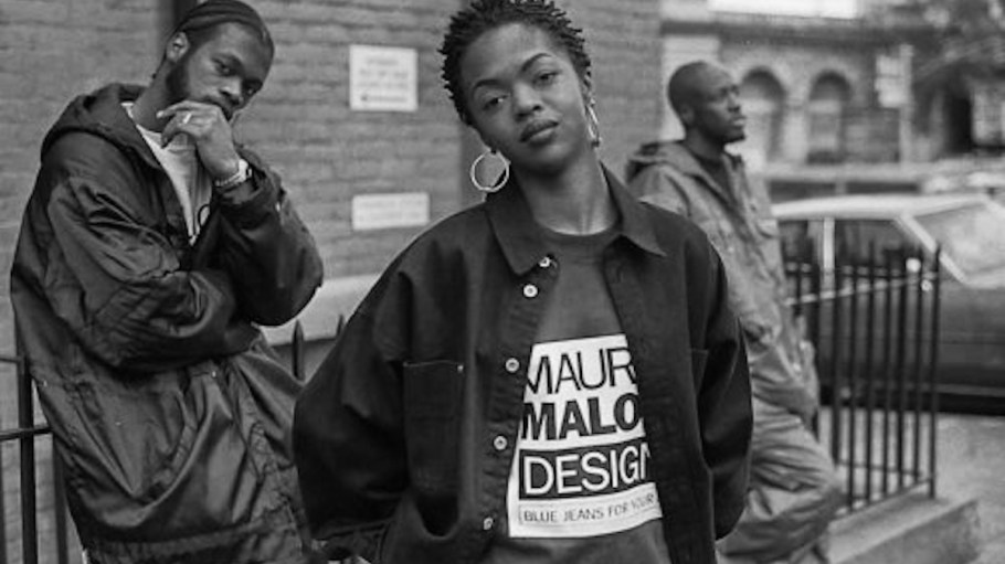 1990s youth hip-hop stars Lauryn Hill wearing Maurice Malone "Blue Jeans For Your Ass" logo T-shirt with Pras Michel and Wyclef Jean of "the Fugees" in the background.