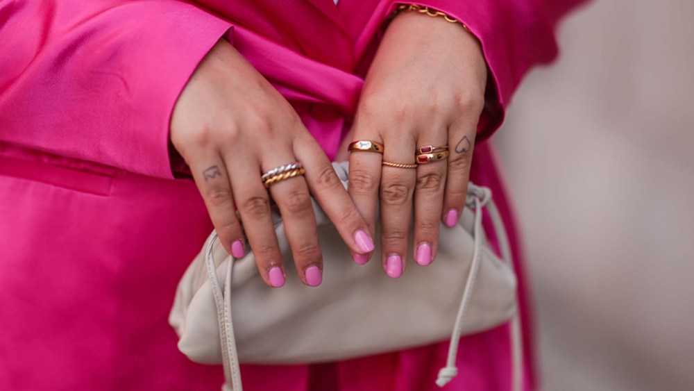 woman wearing pink suit and pink nail polish holding a beige clutch bag