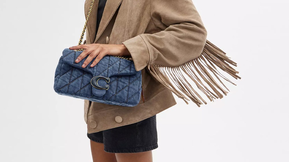 Woman holding Coach denim tabby bag that is back in stock