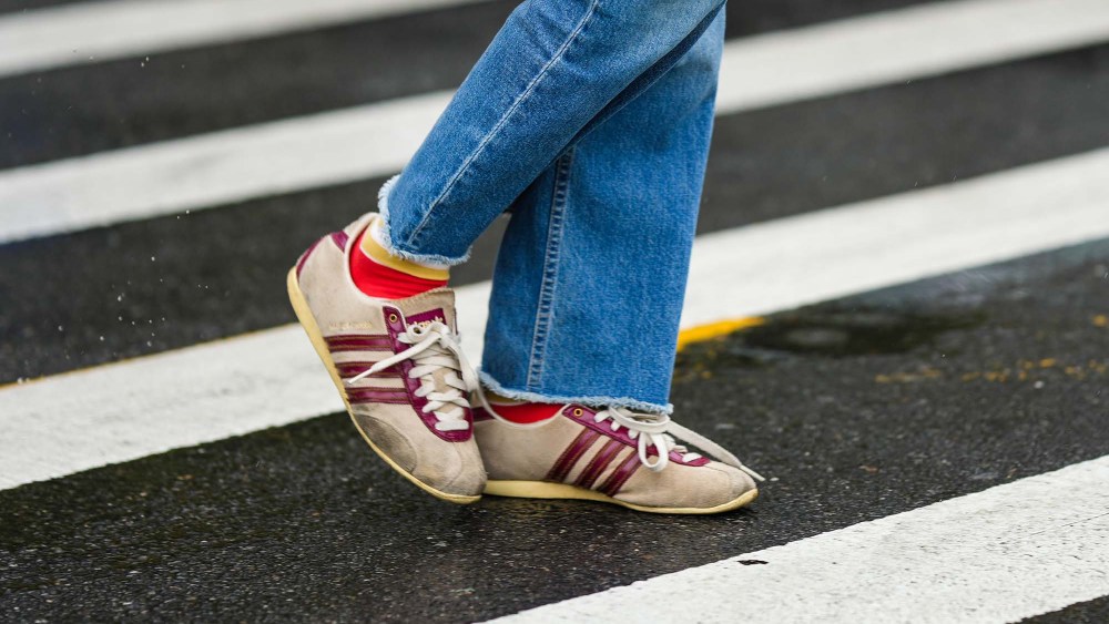 person wears jeans and burgundy striped Adidas sneakers