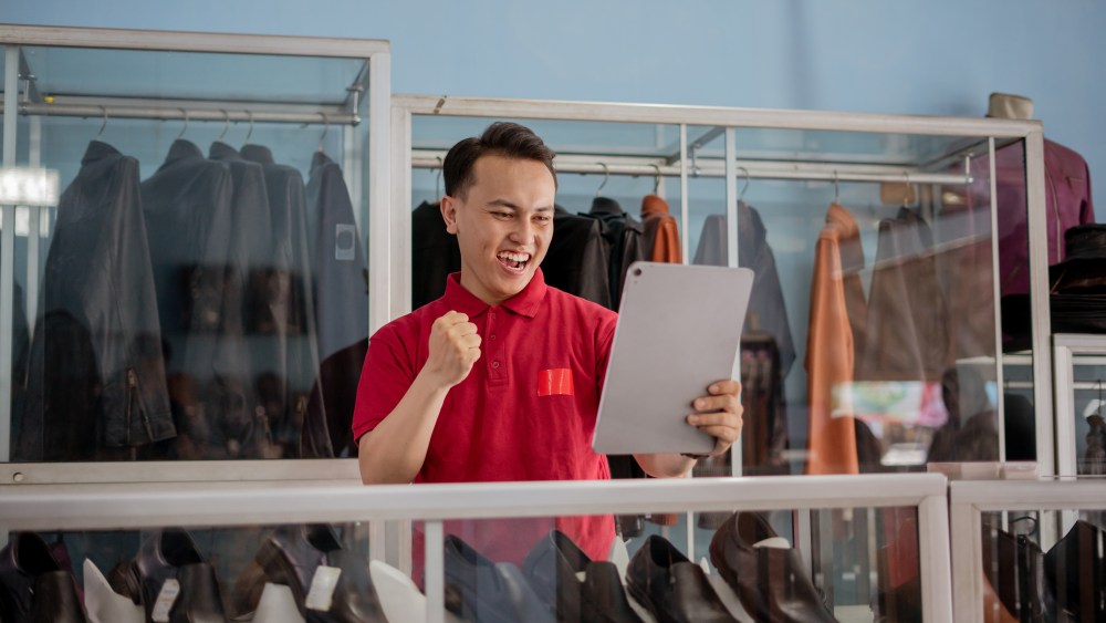 leather shoe salesman celebrating something holding tablet with fist pump gesture