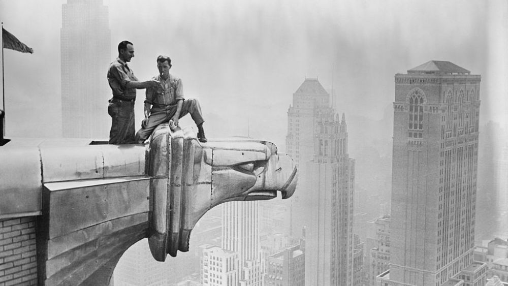 A man lights a fellow worker's cigarette as they take a break on a Chrysler Building gargoyle.